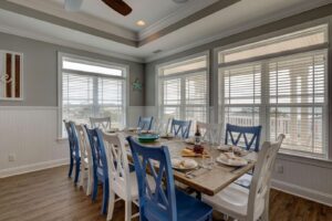 Wooden dining table with chairs in a bright dining room with large windows at Living the Dream
